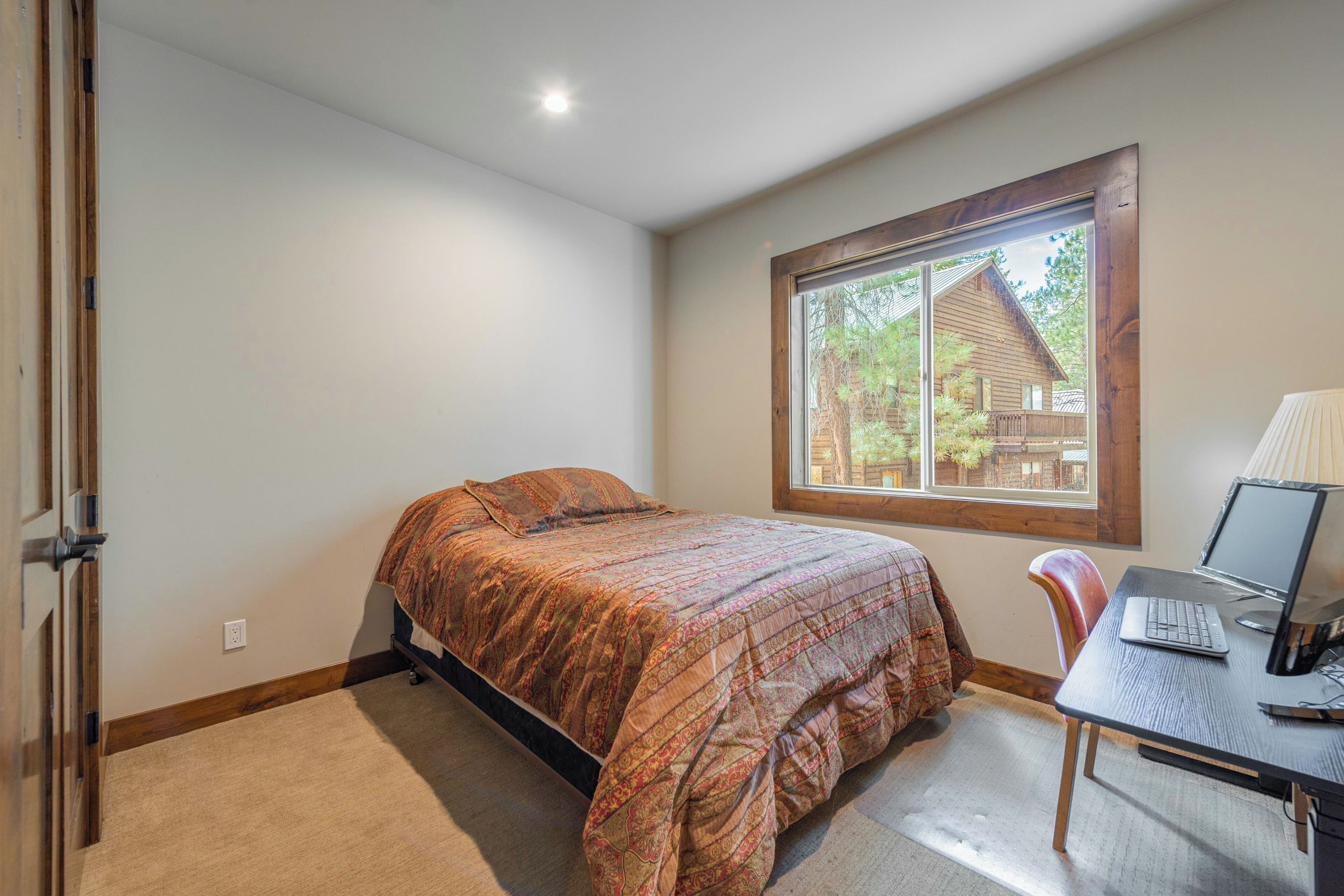Un dormitorio con cama, un escritorio con computadora portátil y una ventana con vista a una cabaña.