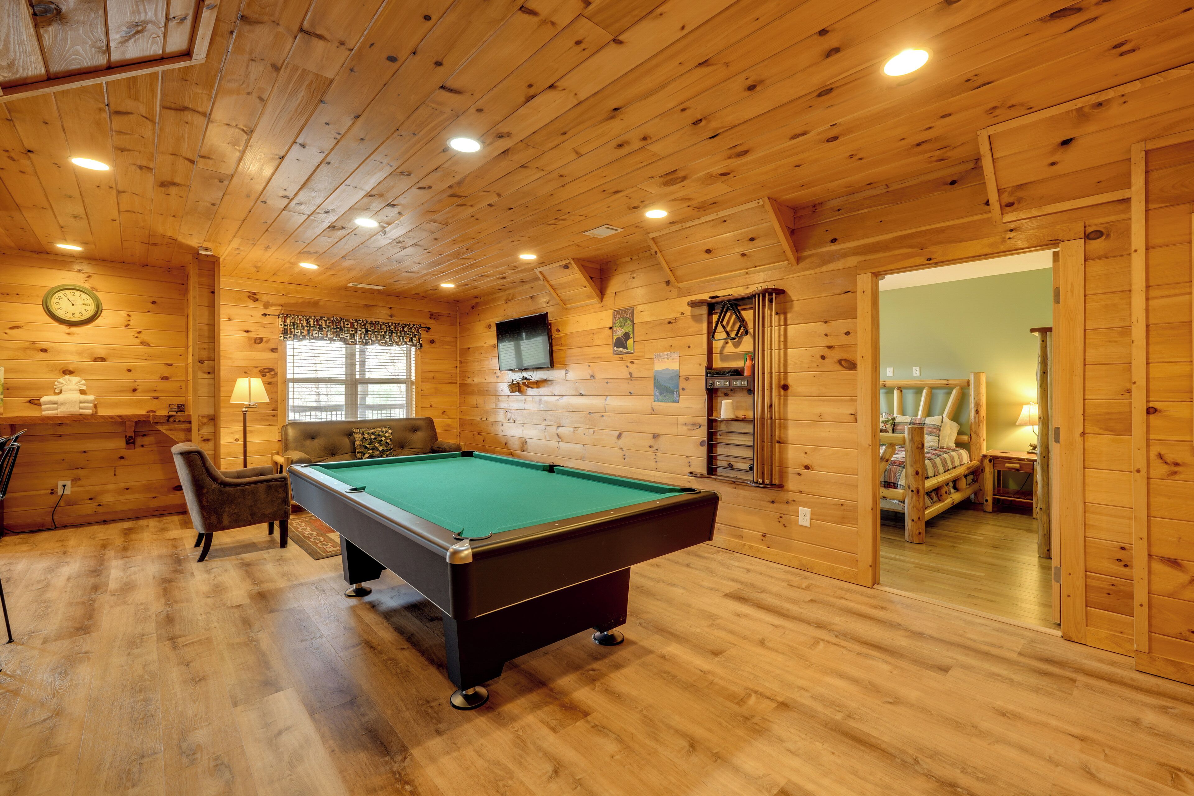A wooden interior with a pool table, a chair, a clock, and a television.