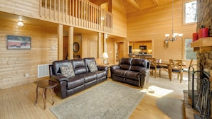 Ein Interieur einer Holzhütte mit Balkon, Ledersofas, einem Essbereich und einem Kamin.