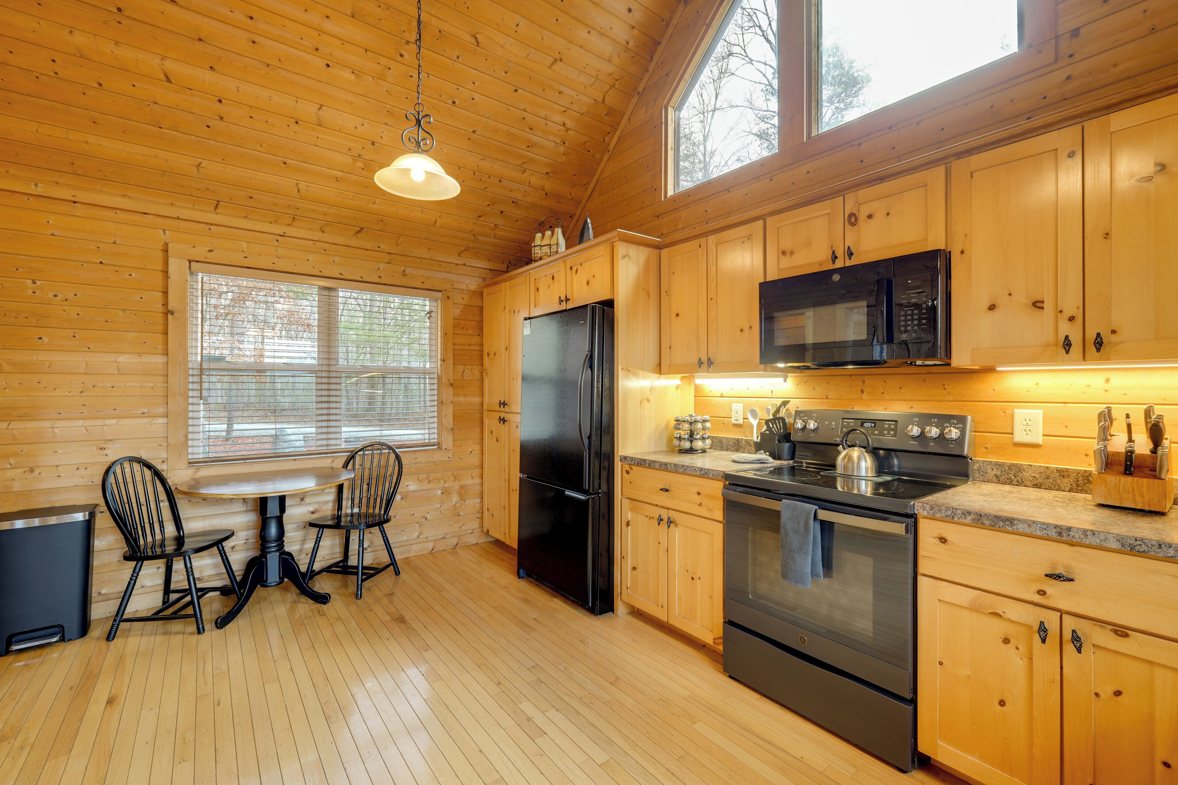 A wooden cabin interior with a kitchen featuring a refrigerator, stove, microwave, and wooden cabinets.