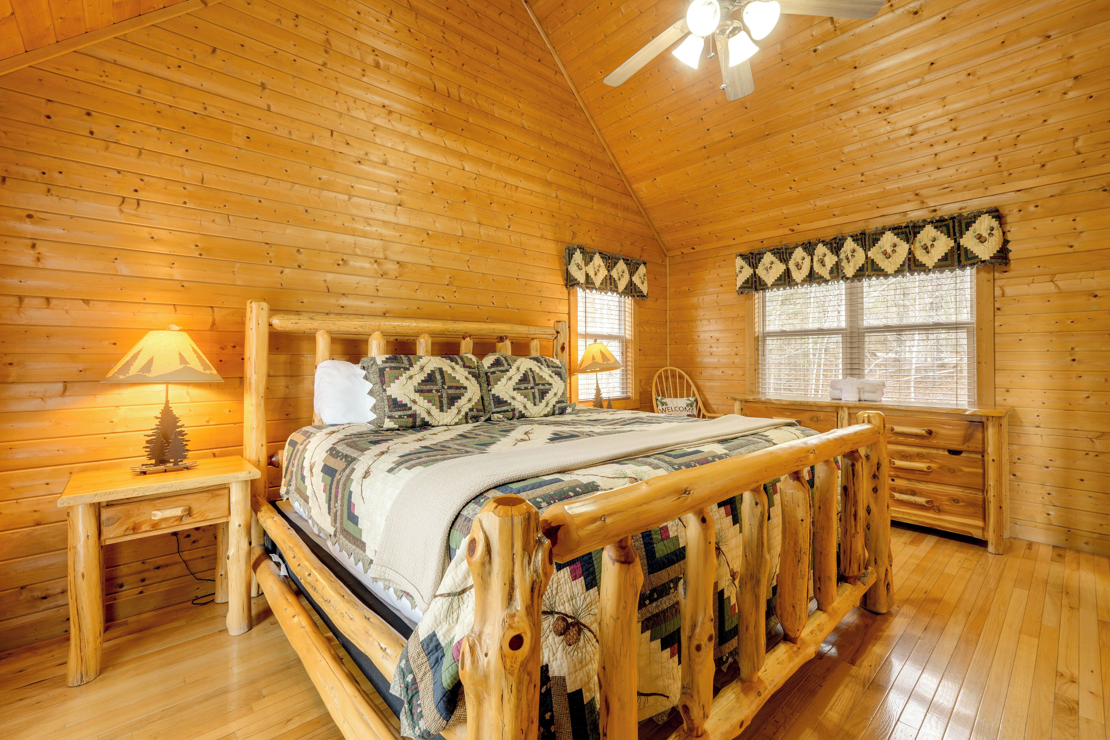 Un dormitorio de cabaña de madera con cama, mesitas de noche, un escritorio y una ventana.