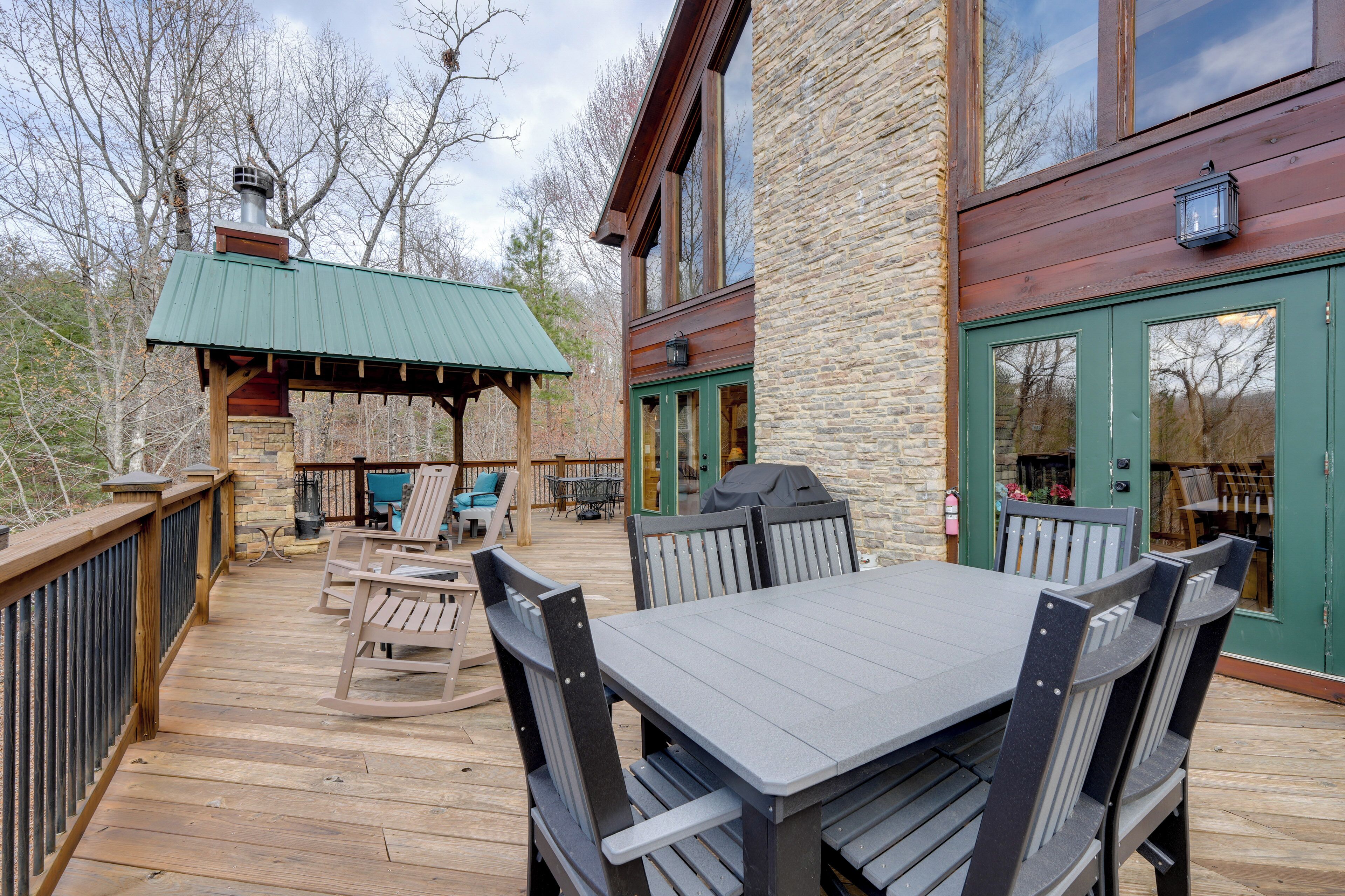 A wooden deck with a table and chairs, a covered seating area, and a stone building with a green door.