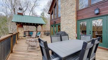 A wooden deck with a table and chairs, a covered seating area, and a stone building with a green door.