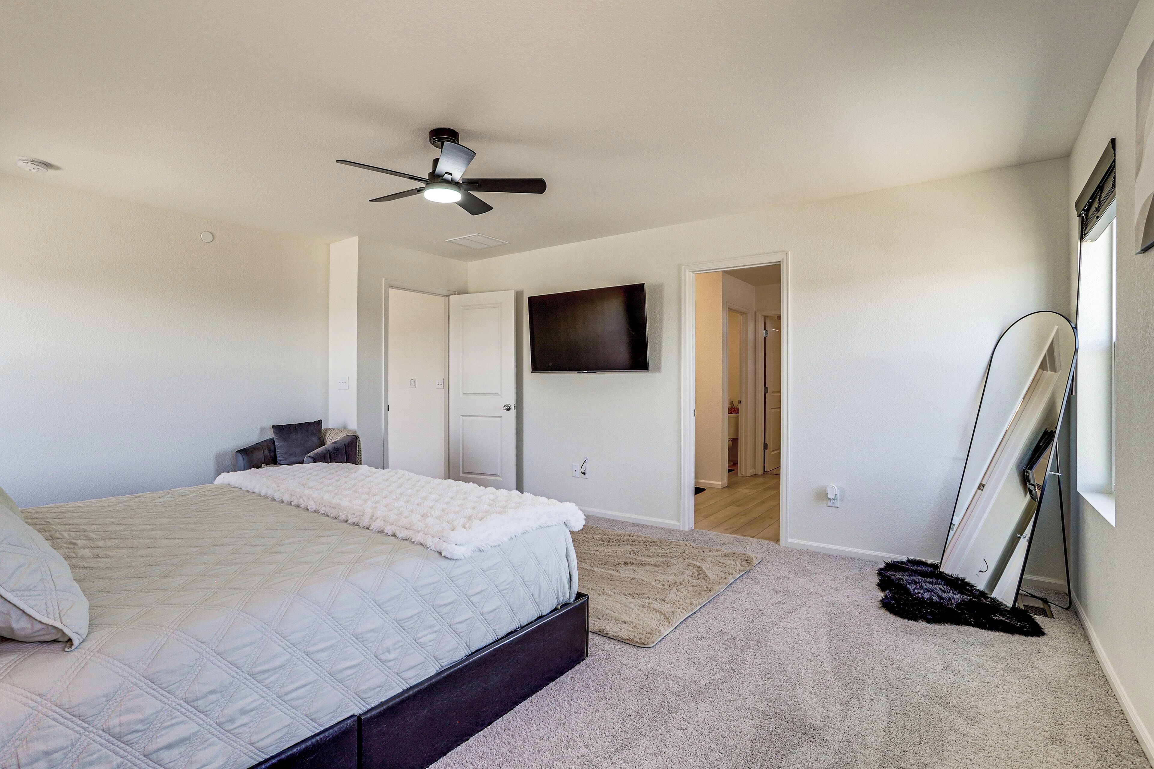 Un dormitorio con cama, ventilador de techo, televisor y puerta que da a otra habitación.