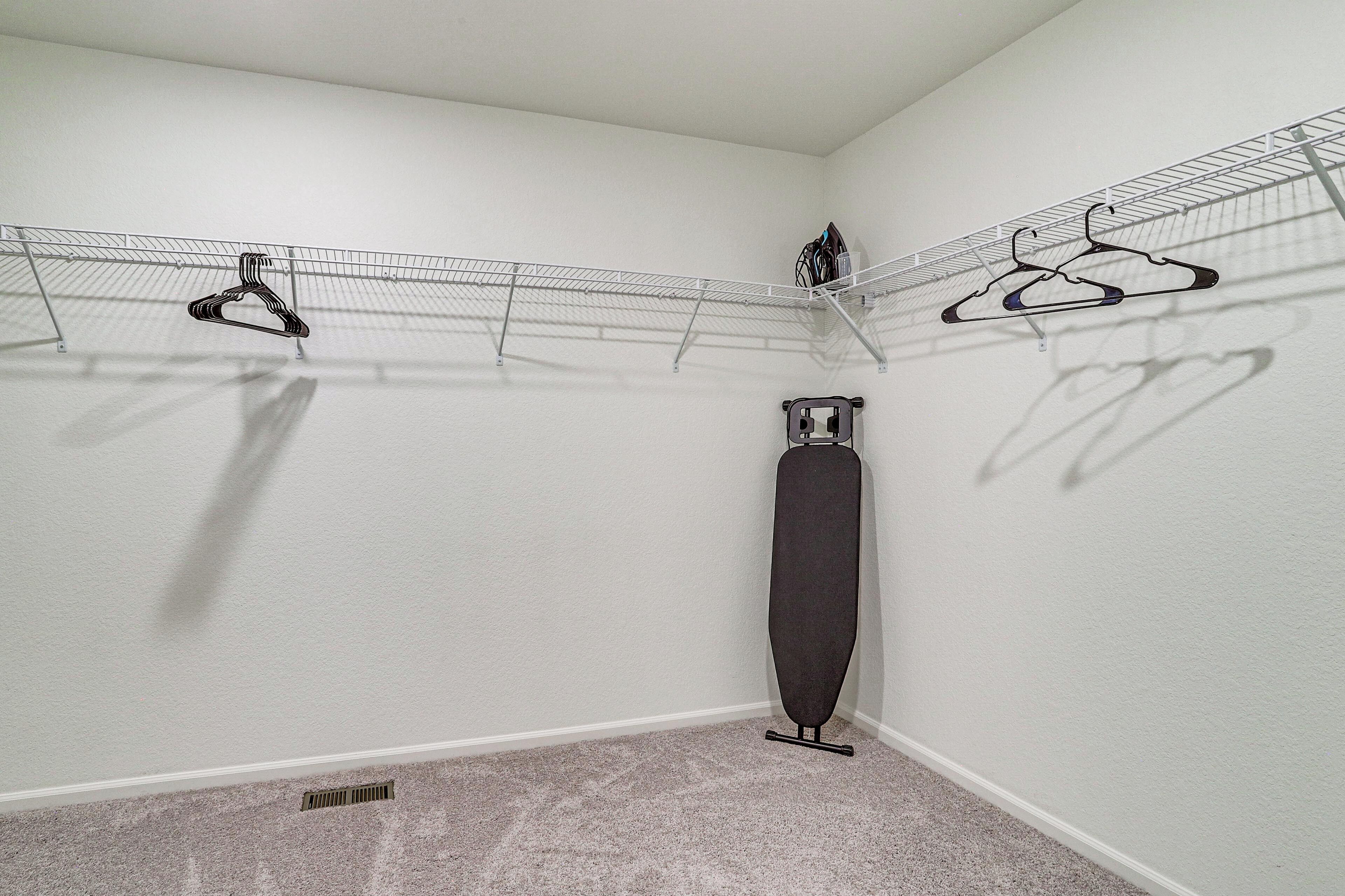 A laundry area with a drying rack, a hanging rack, and a tall ironing board.
