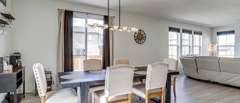 A modern living room with a dining table, chairs, a sofa, and a chandelier.