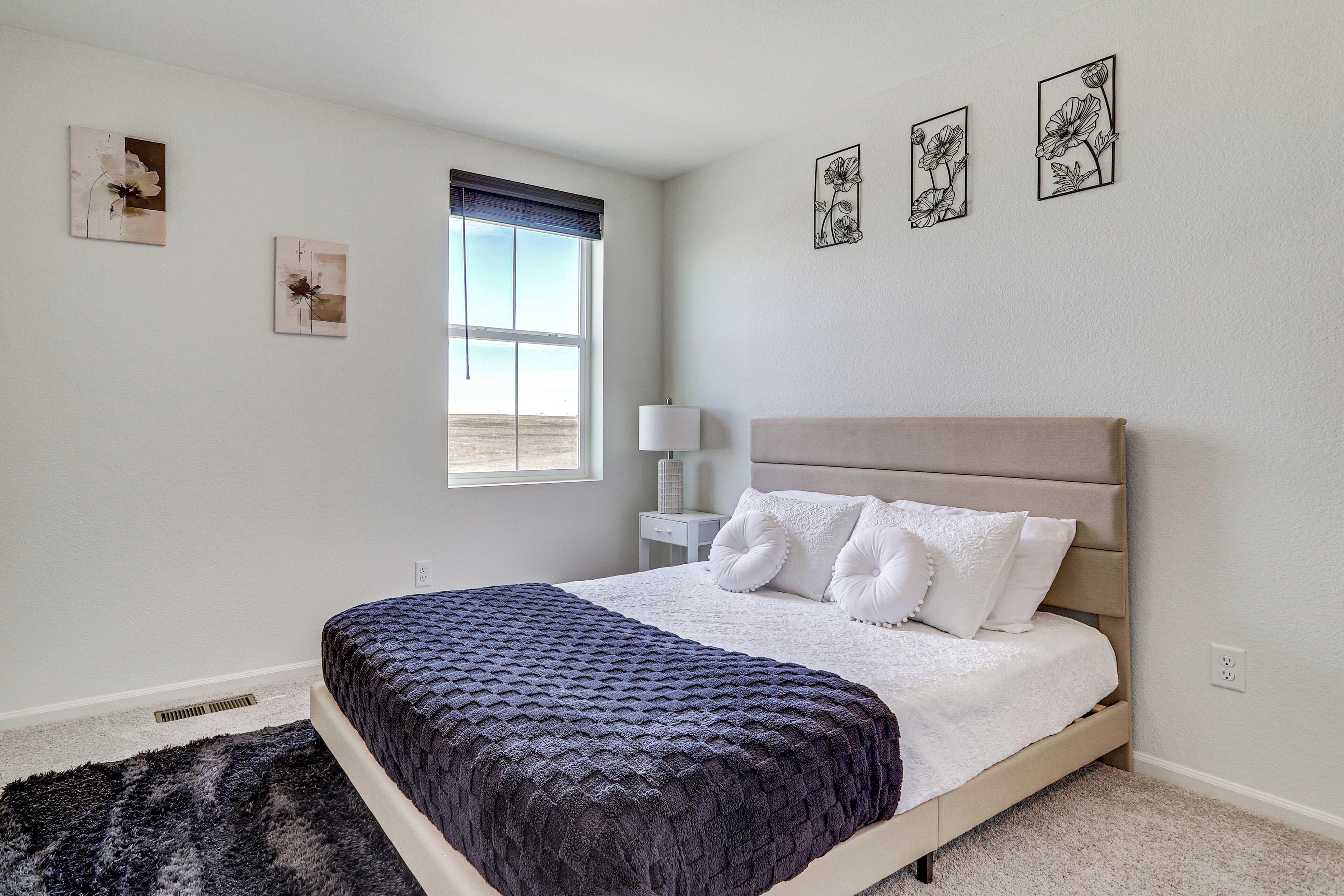 A bedroom with a bed, a window, a nightstand, and wall art.
