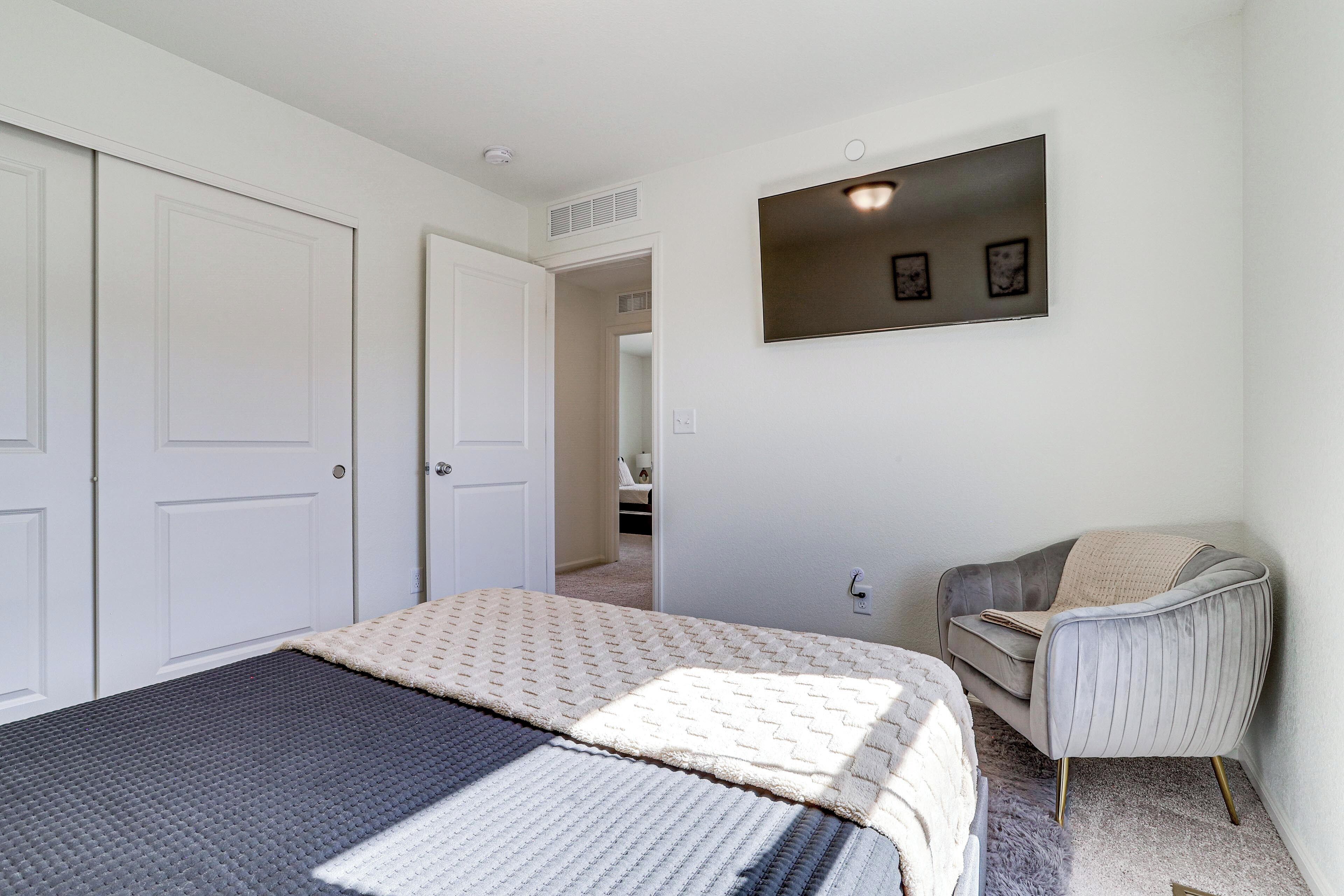 A bedroom with a bed, a chair, a wardrobe, and a wall-mounted picture.