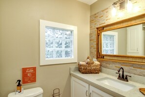 Een badkamer met toilet, wastafel en een grote spiegel. Er hangt een bord met 'DO NOT FLUSH' aan de muur en er staat een mand handdoeken op de aanrecht.