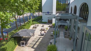 Een buitenruimte met tafels en stoelen, een overdekt gedeelte en een gebouw met een bord waarop 'FLEICHER HOTEL NÜWEGEIN' staat.