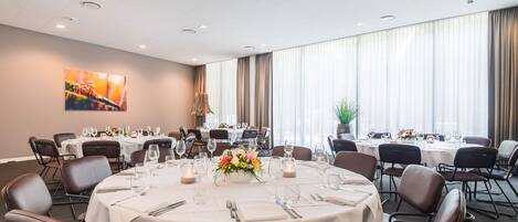Un salón de conferencias con mesas redondas, sillas y un amplio ventanal con cortinas.