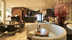 Un moderno vestíbulo de hotel con una zona de estar curva, un bar y un árbol decorativo.