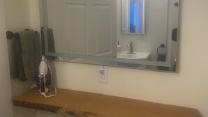 Un baño con un espejo grande, un estante de madera, un perchero y un secador de pelo.