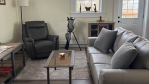 Una sala de estar con un sillón de cuero, un sofá, una mesa de centro, un telescopio y una ventana con adornos.