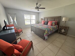 A bedroom with a bed, a desk, two chairs, a ceiling fan, a nightstand, and a window. - 2 Bedroom Condo On The Water in gated Marina and Golf Course Community (Punta Gorda)