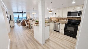A modern kitchen with white cabinets, a black stove, and a large window overlooking a balcony. - Summerchase 305 by Liquid Life (Orange Beach)