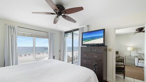 A hotel room with a large bed, a ceiling fan, a TV on a dresser, a balcony with a view of the beach, and a mirror. - Summerchase 305 by Liquid Life (Orange Beach)