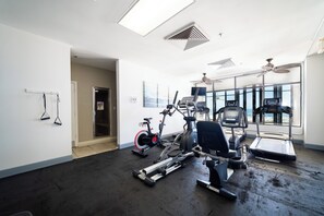 Ein Fitnessraum mit Trainingsgeräten, großen Fenstern und einem Deckenventilator.