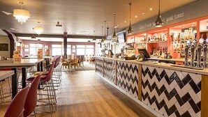 Un espace bar doté d’un comptoir à motifs en chevrons, de tabourets de bar, d’un éclairage suspendu et d’un panneau affichant le menu.