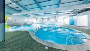 Une piscine intérieure avec des couloirs bien délimités, un espace recouvert d’un gazon synthétique vert et un plafond bleu.