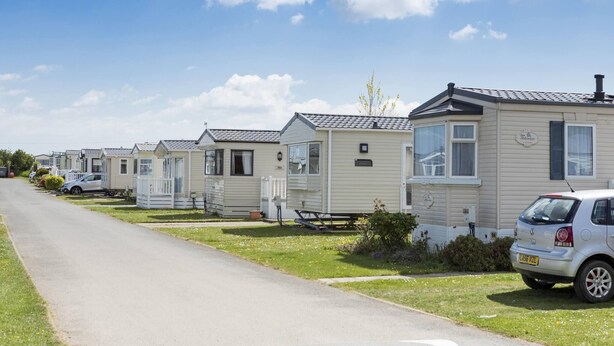 Une rangée de maisons mobiles, avec une route asphaltée devant, chacune ayant une petite voiture garée à côté.