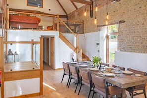 A dining area with a wooden table set for six, a staircase, and a brick wall. - Hillside Barn, Gimingham, Cromer, Norfolk (Gimingham)