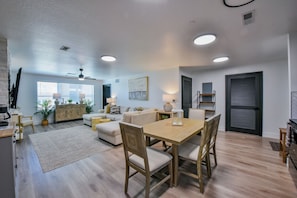 A modern living room with a dining area, a kitchen, and a large window with blinds. - Critter's Cove-Book for graduation & football weekends!  Complex Pool & more! (Tuscaloosa)