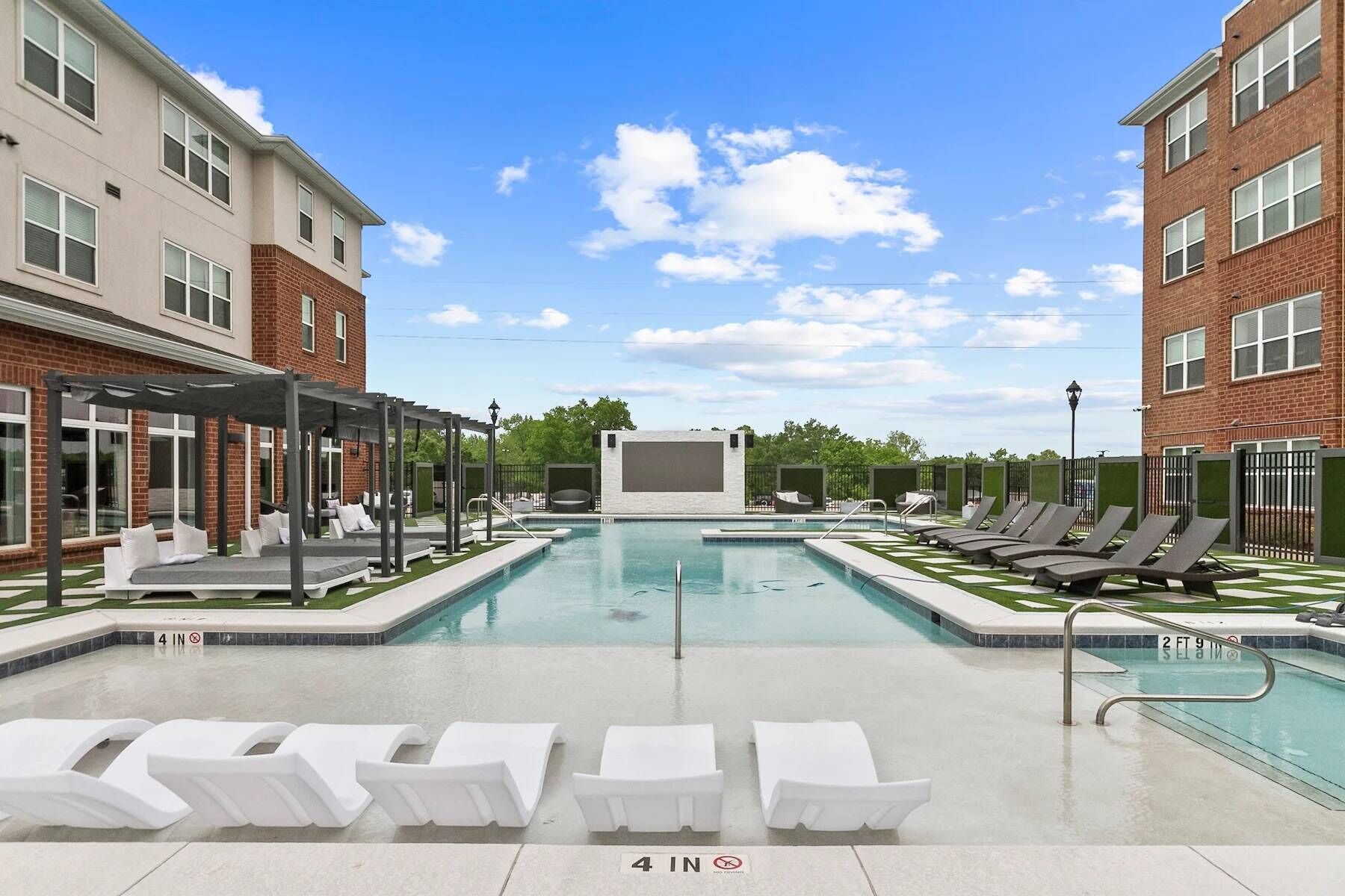 A swimming pool with lounge chairs, a covered seating area, and a clear sky.