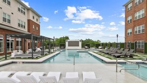 A swimming pool with lounge chairs, a covered seating area, and a clear sky.