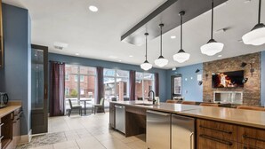 A modern kitchen with a central island, pendant lighting, and a brick accent wall.