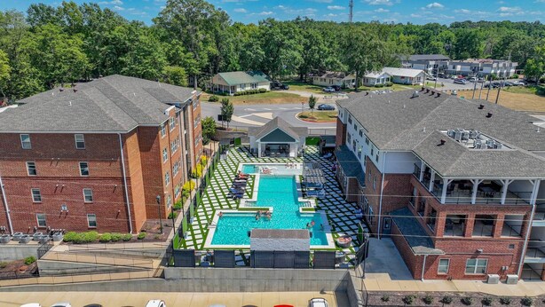A multi-story building with a rooftop pool area, surrounded by greenery and other buildings.