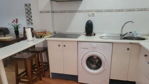 A compact kitchen with a washing machine, a sink, and a small dining area with stools. - Apartment in Almeria With Shared Pool (Vera)