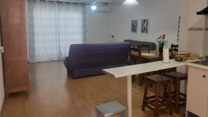 A compact living space with a sofa, dining table, kitchen area, and a trash bin. - Apartment in Almeria With Shared Pool (Vera)