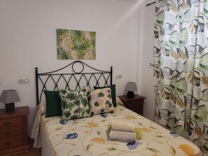 A bed with a floral bedspread, a headboard, two bedside tables with lamps, a wall-mounted power outlet, and a curtain with a leaf pattern. - Apartment in Almeria With Shared Pool (Vera)