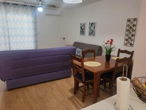 A room with a purple sofa, wooden dining table, chairs, a potted plant, and wall art. - Apartment in Almeria With Shared Pool (Vera)