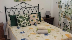 A bedroom with a bed, a nightstand, a lamp, a painting, and a curtain with a leaf pattern. - Apartment in Almeria With Shared Pool (Vera)