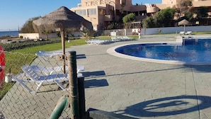A swimming pool with lounge chairs, a thatched structure, and buildings in the background. - Apartment in Almeria With Shared Pool (Vera)