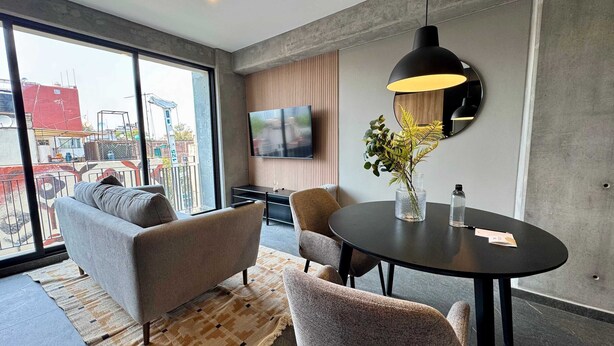A modern living room with a sofa, chairs, a round table, a TV, and a large window with a view of buildings. - w Tasteful 1BR w Private Balcony in Tabacalera (Mexico City)