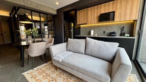 A modern living room with a sofa, chairs, a dining table, and a kitchen area with wooden cabinets and a microwave. - w Tasteful 1BR w Private Balcony in Tabacalera (Mexico City)