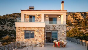 A modern two-story house with a stone facade, a swimming pool, and a dining area with outdoor furniture. - Villa Alexia - Private Pool Panoramic Sea Views (Samos)