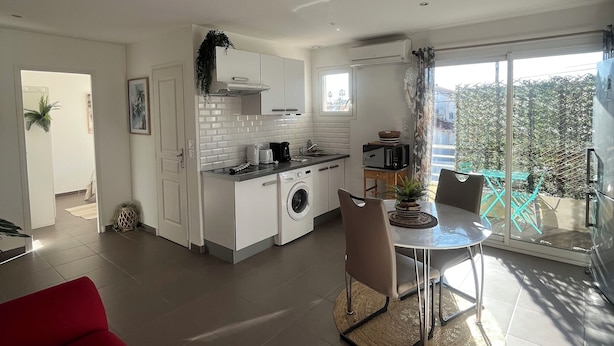 A modern kitchen with a built-in washing machine, a dining area with a table and chairs, and a red sofa. - Le Chic Azuréen (Villeneuve-Loubet)