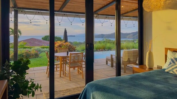 Camera da letto con un'ampia porta scorrevole in vetro che dà su un patio esterno con piscina e zona pranzo.