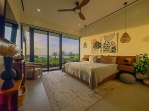 Ein Schlafzimmer mit einem Bett, einem Deckenventilator, einem großen Fenster und Blick auf Grünflächen.