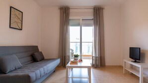 A modern living room with a grey sofa, a white coffee table, a television on a stand, and a balcony with curtains. - Vacation Apartment in Roquetas de Mar (Roquetas de Mar)