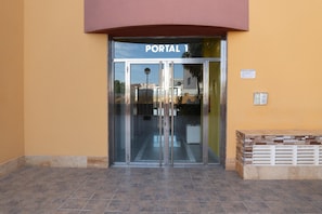 A building entrance with a glass door labeled 'PORTAL,' a small outdoor seating area, and a wall-mounted light fixture. - Vacation Apartment in Roquetas de Mar (Roquetas de Mar)