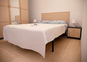 A neatly made bed with a white bedspread, a bedside table with a lamp, and a wooden wardrobe. - Vacation Apartment in Roquetas de Mar (Roquetas de Mar)