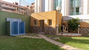 A building with a stone facade, a small entrance, and a paved pathway leading to a seating area with a statue. - Vacation Apartment in Roquetas de Mar (Roquetas de Mar)