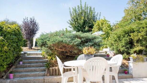 Eine Terrasse mit weißen Plastikstühlen und einem Tisch, umgeben von Steinstufen und Grünpflanzen.