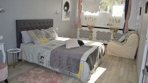 Ein Schlafzimmer mit einem Bett, einem kleinen Nachttisch, einem Stuhl und einem Fenster mit Vorhängen.