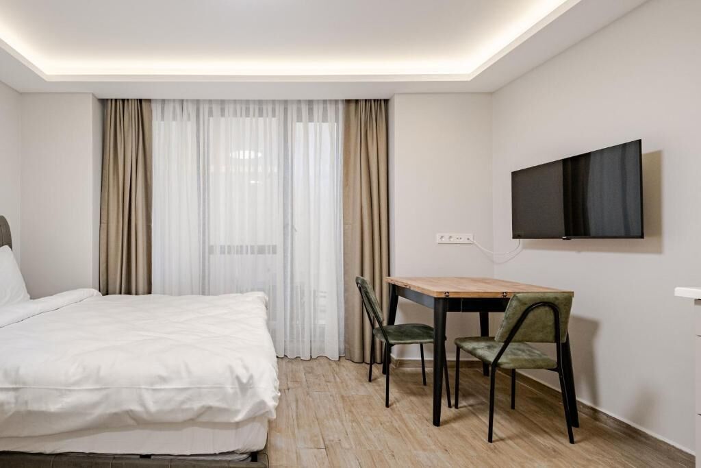 Una habitación de hotel con una cama, un escritorio con dos sillas, un televisor montado en la pared y una ventana con cortinas.